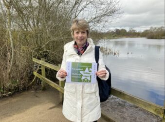 Female holding a certificate standing in front of a lake