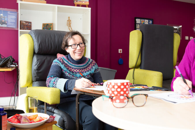 Female sitting in a chair with a cup and colouring on the table