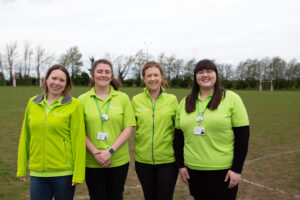 4 females wearing green fleeces smiling at the camera, outside
