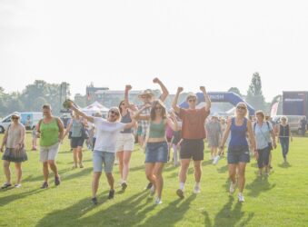 Males and females on a green area with their hands in the air, wearing shorts.