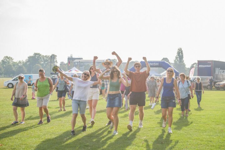 Males and females on a green area with their hands in the air, wearing shorts.