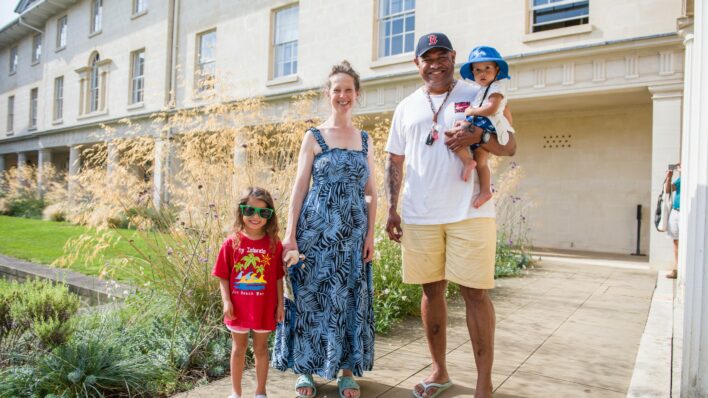 Male and female and 2 children standing near a building looking at the camera