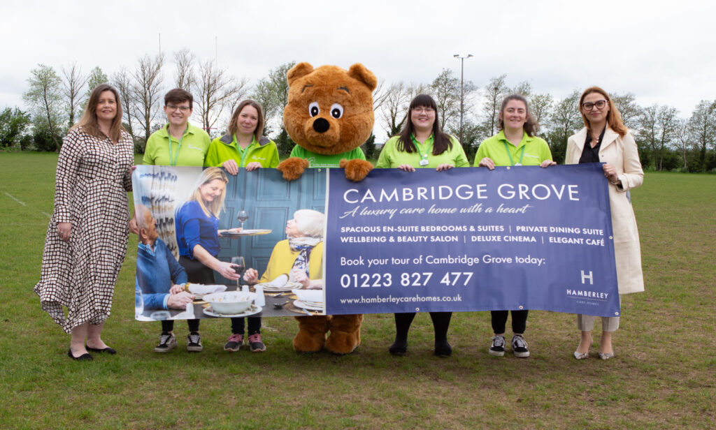 6 females and a life sized bear holding a large banner outside 