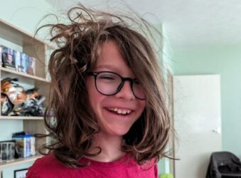 Boy smiling at camera in red t shirt and glasses with long broen hair