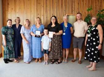 Group of adults and 1 child smiling at the camera, holding an award