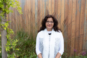 Female wearing white standing in front of a wooden shed outside