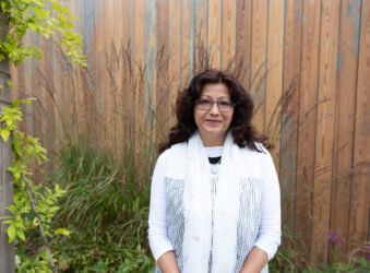 Female wearing white standing in front of a wooden shed outside