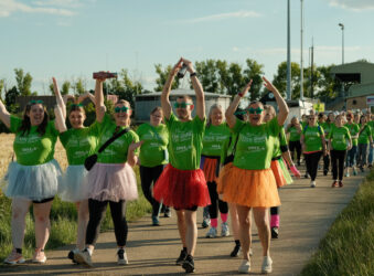 Males and females wearing colorful tutus walking and arms in the air