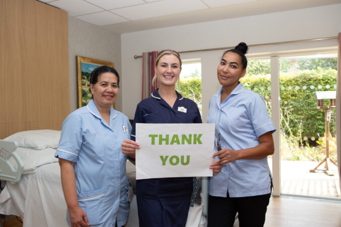 3 nurses holding a Thank you sign in front of a bed