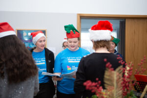 3 females in red Santa hats singing 