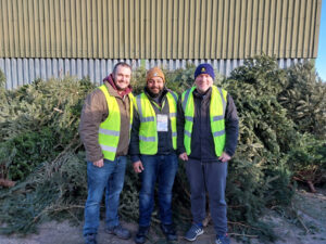 3 males wearing high vis standing in front of Christmas trees