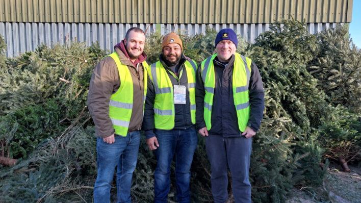 3 males wearing high vis standing in front of Christmas trees