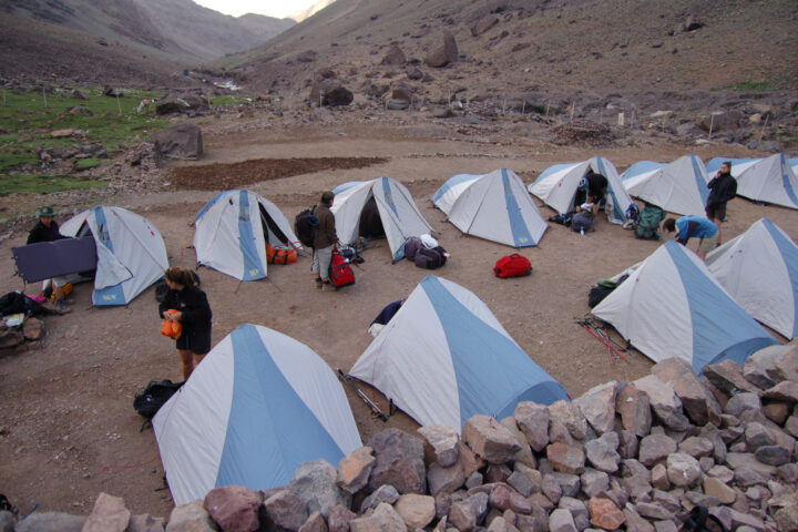 Blue and white tents at the bottom of a mountain