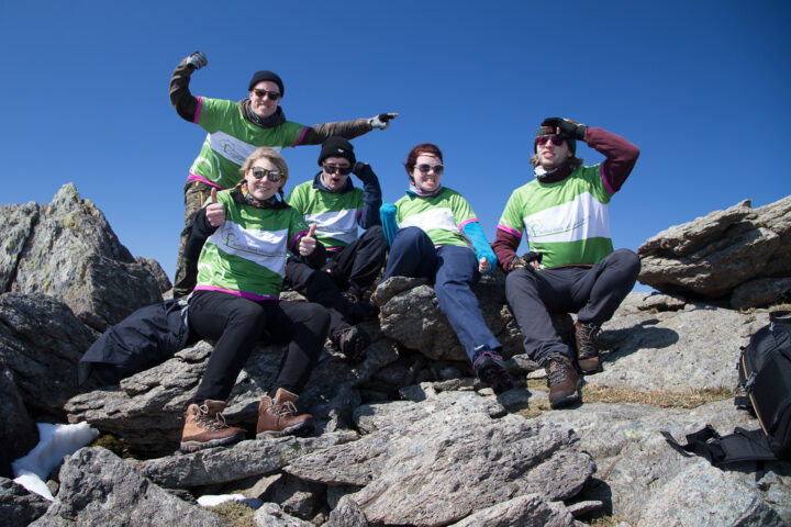 5 people on green and white tops on a mountain top