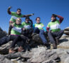 5 people on green and white tops on a mountain top