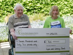 Lady and man in the hospice garden with giant cheque