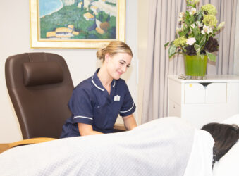 Female nurse smiling at a female in a bed