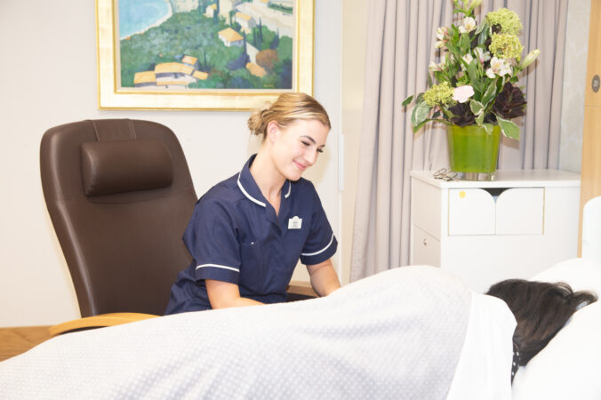 Female nurse smiling at a female in a bed