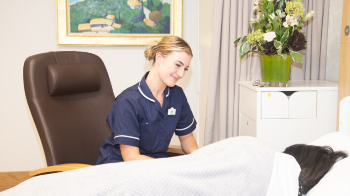 Female nurse smiling at a female in a bed
