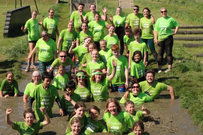 35 people in green Arthur t-shirts in muddy water smiling at camera