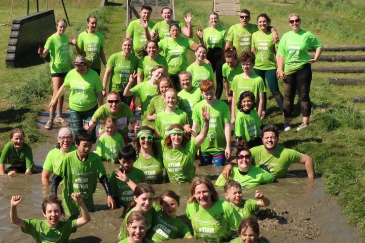 35 people in green Arthur t-shirts in muddy water smiling at camera