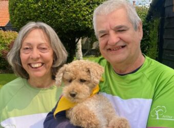 man and lady smiling at the camera in Arthur rank tshirts holding small brown dog