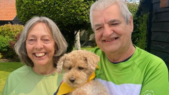man and lady smiling at the camera in Arthur rank tshirts holding small brown dog