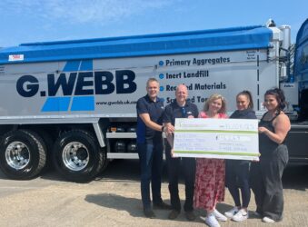 Male and females with a large cheque standing in front of a lorry
