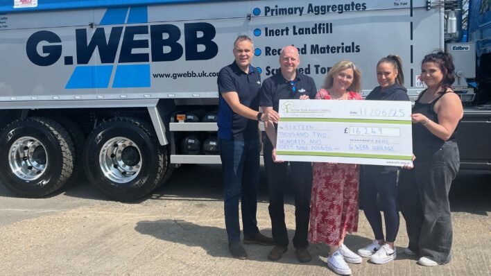 Male and females with a large cheque standing in front of a lorry