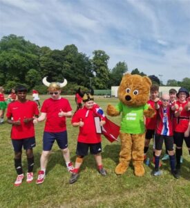 Arthur bear on grass with 7 teenage boys in red tshirts