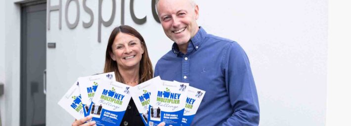 Female and male holding Money Multiplier Challenge blue leaflets outside hospice sign