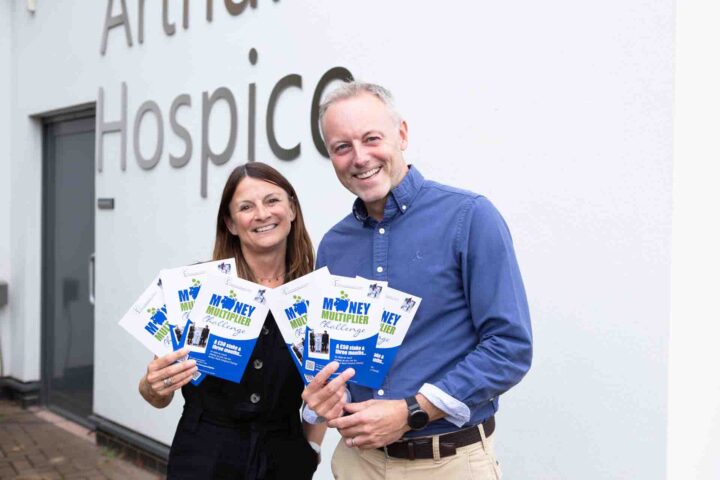 Female and male holding Money Multiplier Challenge blue leaflets outside hospice sign