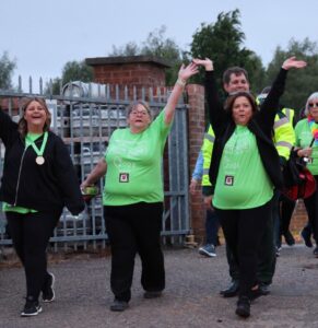 Three females walking in green t shirts - hands in the air