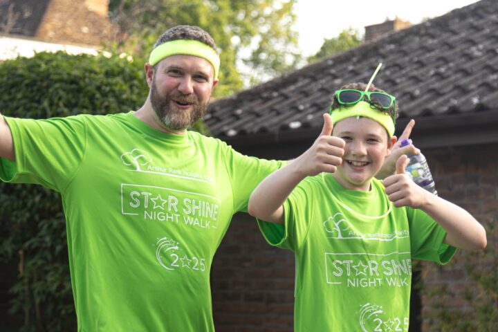 Man and teen on the walk wearing bright green star shine tshirts. Man has arms out wide and teen has thumbs up.