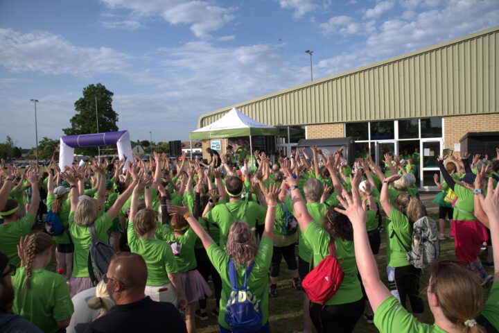 Large group of people in bright green tshirts with their back to the camera and arms raised in the air cheering.