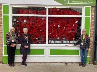 3 females outside a shop with red crocheted poppies