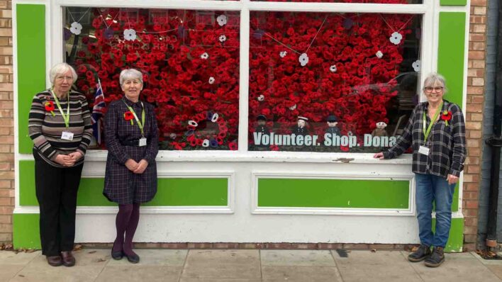 3 females outside a shop with red crocheted poppies