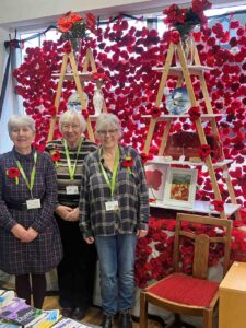 3 females standing near crocheted red poppies