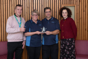 2 Males and 2 females wearing blue tshirts holding a glass award