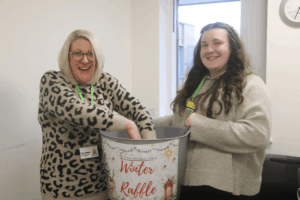 Two women are smiling, one is reaching into a tub for a raffle ticket