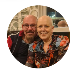 Male and female smiling at the camera. Female with no hair.