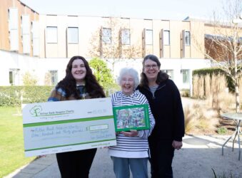 3 females holding a jigsaw puzzle outside in front of a large building
