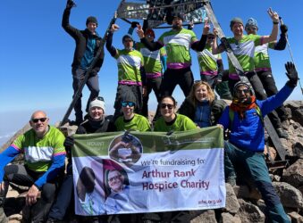 Adults on top of mountain holding Arthur Rank Hospice Charity green banner