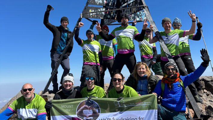 Adults on top of mountain holding Arthur Rank Hospice Charity green banner