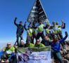 Adults on top of mountain holding Arthur Rank Hospice Charity green banner