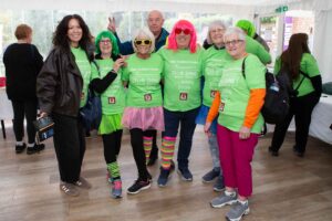 Males and females wearing green and glasses and brightly coloured wigs
