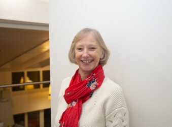 Female smiling at the camera wearing a white jumper and pink scarf