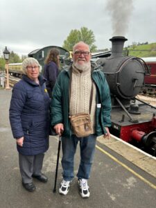 Male and female smiling at the camera in front of a steam train