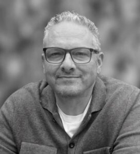 black and white portrait syle photo of man looking and camera around 50 in glasses