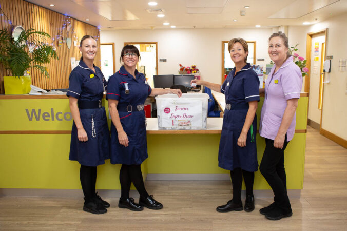 Four females in nurses uniforms picking out a winning raffle ticket.